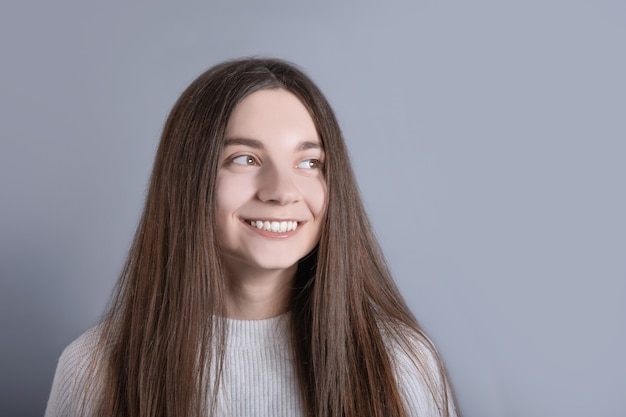 Het jonge mooie vrouwenportret met donker haar dat witte sweater draagt, kijkt weg met een lichte glimlach