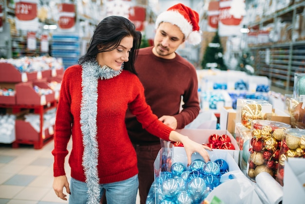 Het jonge paar kiest kerstboomspeelgoed in winkel