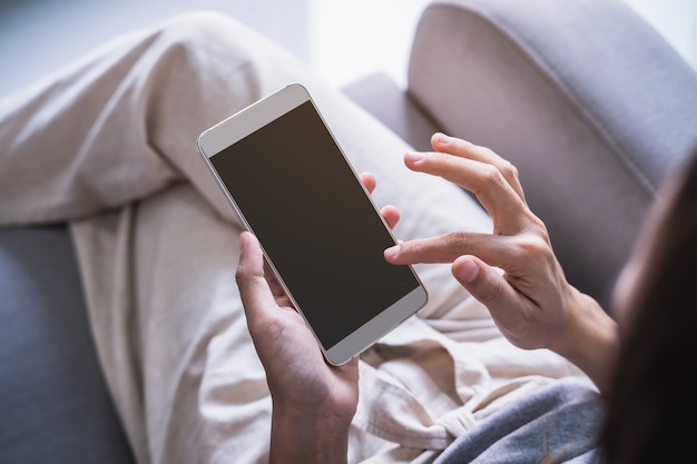 Het jonge vrouw siiting op bank en thuis het gebruiken van slimme telefoon