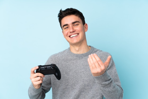 Het Kaukasische de mens van de tiener spelen met een videospellingscontrolemechanisme dat op blauwe achtergrond wordt geïsoleerd die uitnodigt om met hand te komen. Blij dat je bent gekomen