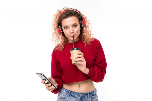 Het Kaukasische meisje met krullend eerlijk haar drinkt koffie, luistert naar muziek en sprekend met vrienden, geïsoleerd portret