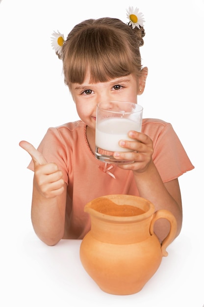 Het kind drinkt melk en verheugt zich Meisje in een oranje T-shirt drinkt verse melk op een witte achtergrond