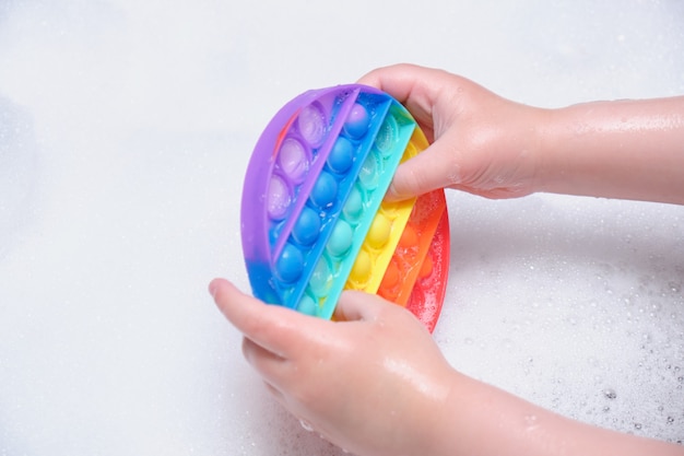 Foto het kind houdt een anti-stressspeeltje met siliconen bubbels vast en laat het in zeepachtig schuim in de badkamer vallen