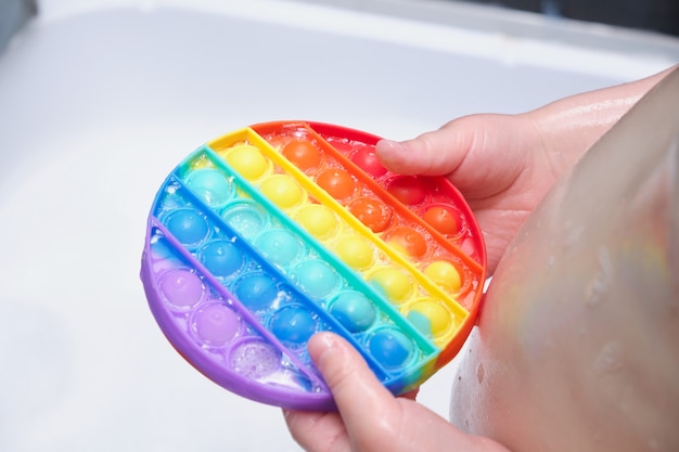 Het kind houdt een anti-stressspeeltje met siliconen bubbels vast en laat het in zeepachtig schuim in de badkamer vallen