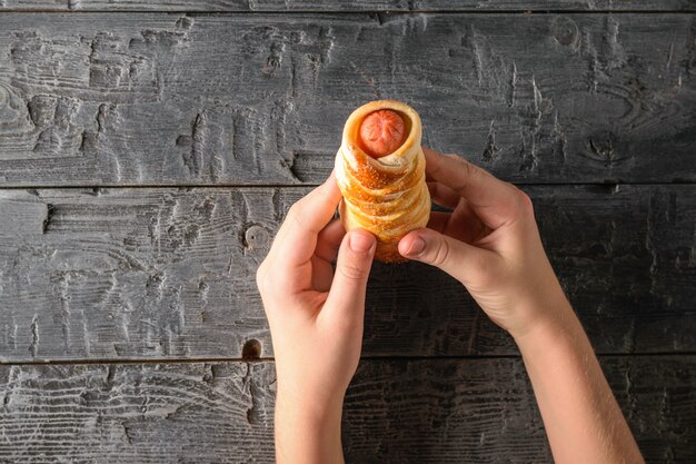 Het kind houdt een verse zelfgemaakte worst in het deeg boven een zwarte houten tafel. Het uitzicht vanaf de top.