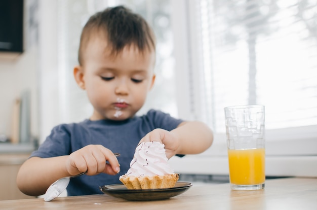 Het kind in de keuken eet een cake met slagroom