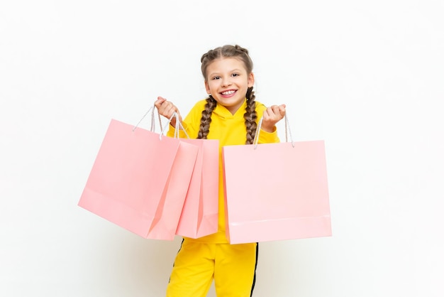 Het kind is blij met nieuwe aankopen Winkelen voor kinderen Een mooi meisje in een geel trainingspak houdt papieren zakken vast