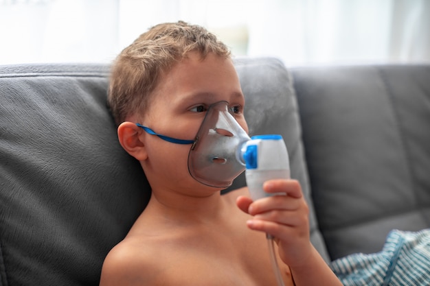 Het kind maakt thuis inhalatieverstuiver. op het gezicht het dragen van een maskervernevelaar die door damp gespoten medicijn in de longen van de patiënt inhaleert. behandeling van de luchtwegen met de verstuiver ingalatia