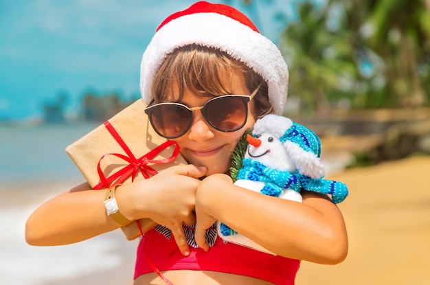 Het kind met kerstmanhoed en zonnebril het houden stelt bij het strand voor