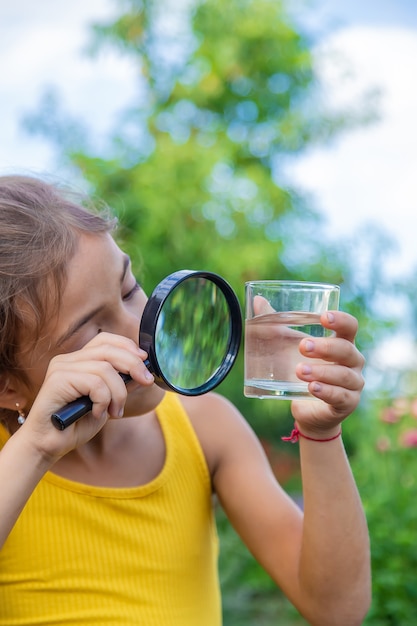 Het kind onderzoekt een glas water met een vergrootglas. Selectieve aandacht.