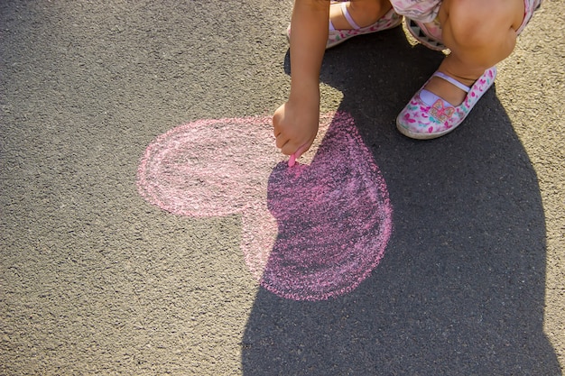 Het kind schildert krijt op het asfalthart. Selectieve aandacht.