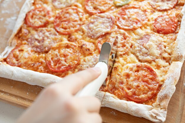 Het kind snijdt pizza met een rolsnijder dicht omhoog