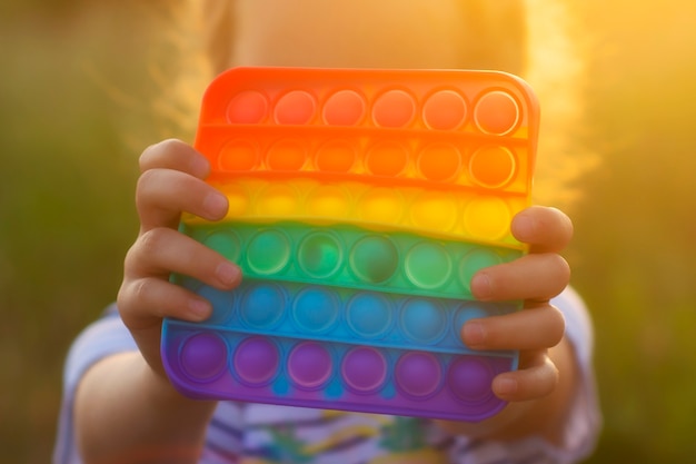 Het kind speelt met een kleurrijk regenboogspel poppit. Siliconen fidget close-up.