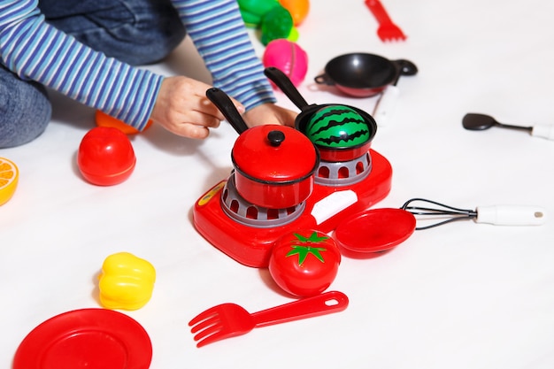 Het kind speelt met gesneden plastic groenten en fruit met klittenband, kookt voedsel op een speelgoedfornuis in een kom. Koken voor kinderen, een meisje leert koken. Witte achtergrond, close-up, concept.