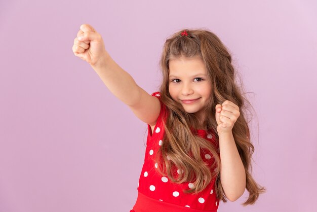 Het kind steekt zijn hand op als teken van succes op een roze achtergrond