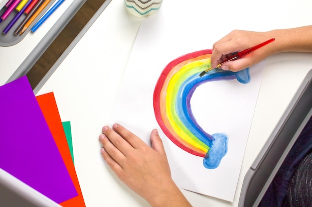 Het kind tekent een regenboog De handen van kinderen houden kleurpotloden vast en tekenen een tekening