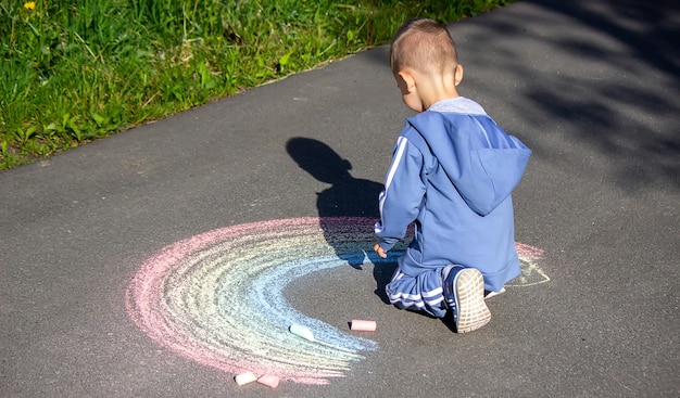 Het kind tekent met krijt de kleuren van de regenboog op het asfalt