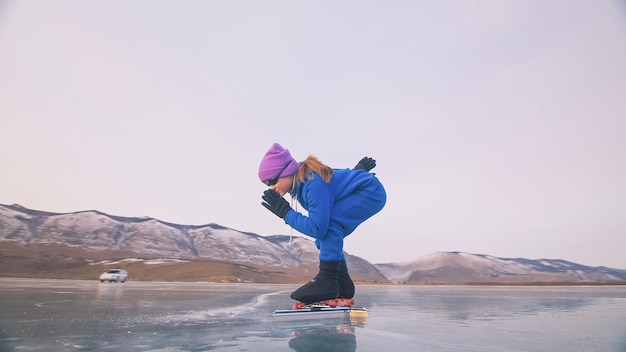 Het kind traint op schaatsen. De atleet aan de start, in een sportieve houding. Het jonge meisje schaatst in de winter in sportkleding, sportbril.