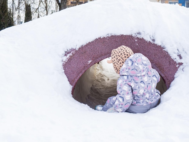 Het kind vermaakt zich in de winter op de speelplaats