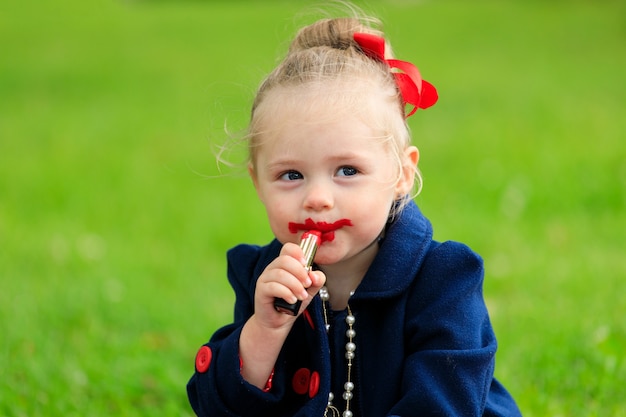 Het kind zit en schildert zijn lippen met rode lippenstift