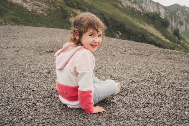 Het kind zit in de bergen en geniet van het uitzicht een baby in een hoodie en jeans zit op de grond...