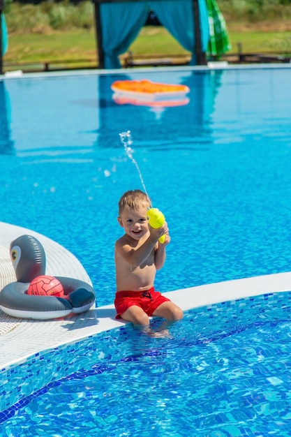 Het kind zit in de buurt van het zwembad wordt gespeeld met een waterpistool. selectieve focus