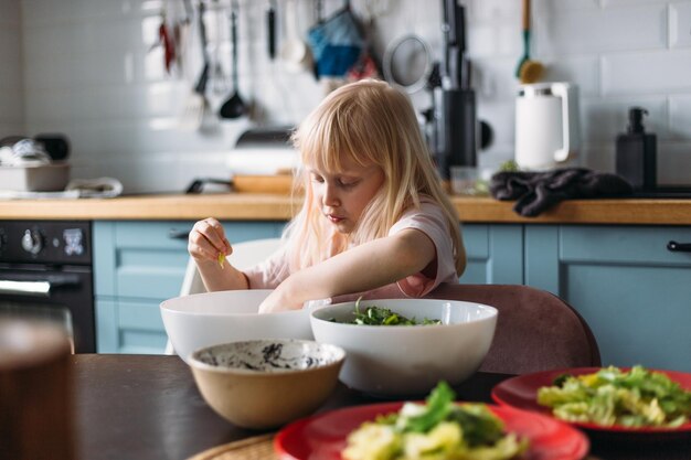 Foto het kleine blonde meisje helpt het eten klaar te maken in de keuken.