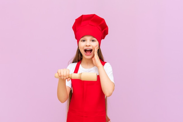 Het kleine chef-kokmeisje opende haar mond van verbazing en glimlacht babybakker op roze geïsoleerde achtergrond