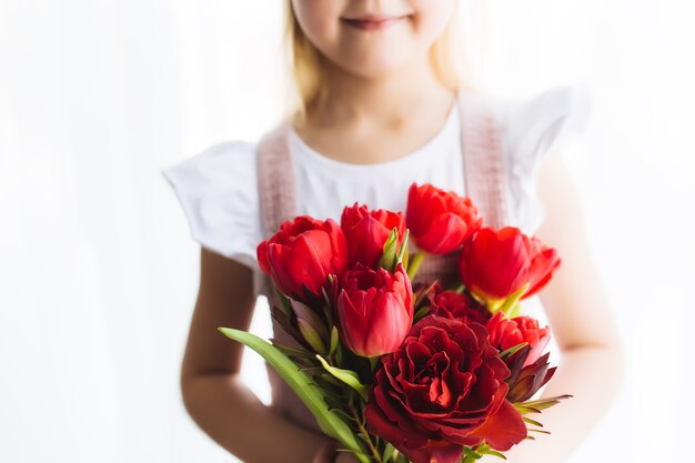 Het kleine glimlachende boeket van de meisjesholding van rode tulpenbloemen. Concept voor wenskaart