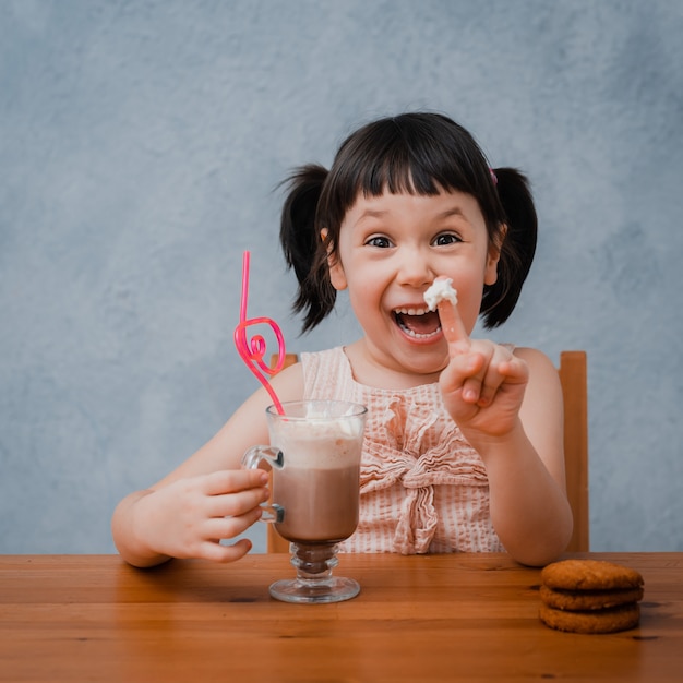 Het kleine kindmeisje drinkt hete chocolade of cacao met koekjes door een cocktailbuis.