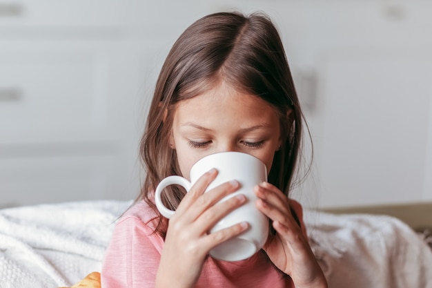 Het kleine meisje drinkt uit een witte mok. Close-up portret