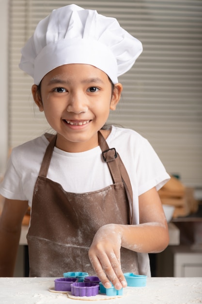 Het kleine meisje droeg een witte koksmuts en een bruin schort om koekjes te maken