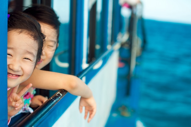 Het kleine meisje glimlacht verlegen naar de camera en opent het raam in de boot op de koele zomerzee.