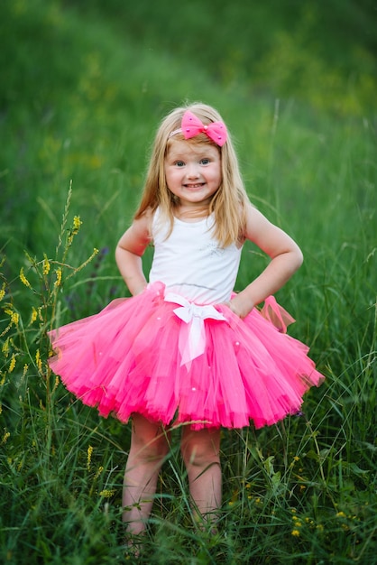 Foto het kleine meisje in een roze jurk loopt blootsvoets op het groene gras in het veld portret van een gelukkige kindprinses in een park