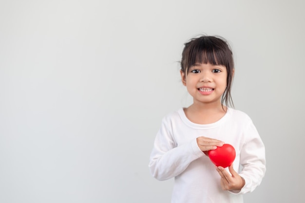 Het kleine meisje in een wit overhemd met een rood hart op een witte achtergrond. Wenskaarten voor valentijnsdag, moederdag, vaderdag.