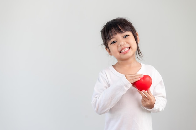 Het kleine meisje in een wit overhemd met een rood hart op een witte achtergrond. Wenskaarten voor valentijnsdag, moederdag, vaderdag.