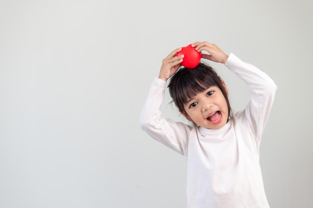 Het kleine meisje in een wit overhemd met een rood hart op een witte achtergrond. Wenskaarten voor valentijnsdag, moederdag, vaderdag.