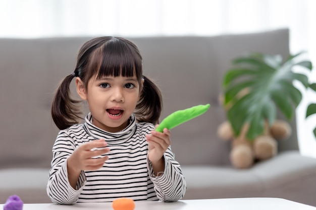 Het kleine meisje leert kleurrijk deeg te gebruiken in een goed verlichte kamer