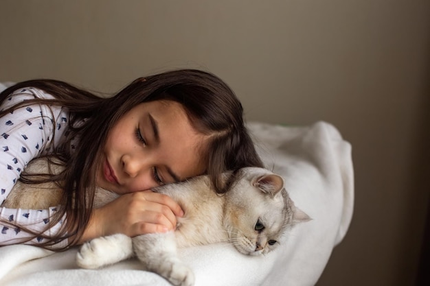 Het kleine meisje ligt met een witte kat op het bed