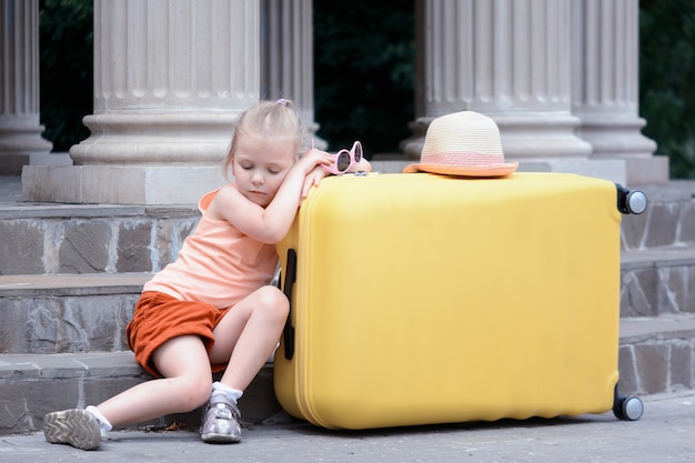 Het kleine meisje viel in slaap op een grote gele koffer. Een schattige baby is het reizen beu.