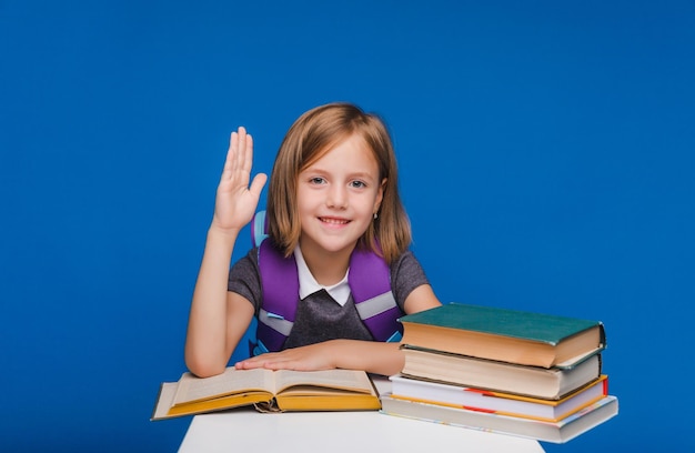 Het kleine schoolmeisje stak haar hand op om de vraag te beantwoorden: een schoolmeisje met boeken op een blauwe achtergrond