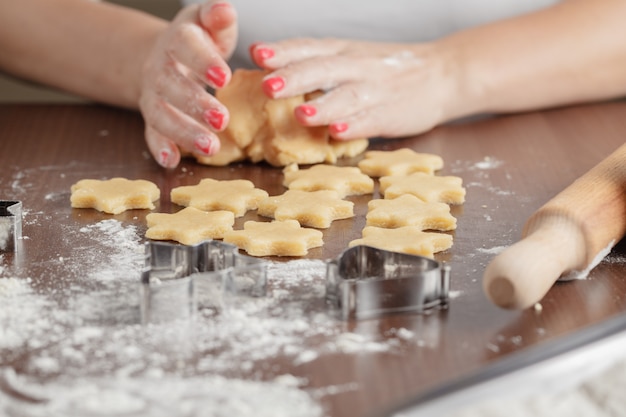 Het koken en huisconcept - sluit omhoog van vrouwelijke handen thuis makend koekjes van vers deeg