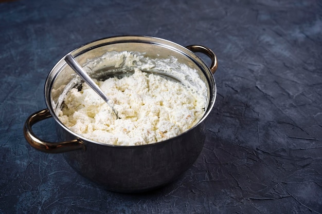 Het koken van heerlijke zelfgemaakte kwark in een pan op de tafel close-up zuivelproducten zijn een gezonde voorbereiding van een kwarkschotel met rozijnen en amandelen getextureerde voedselachtergrond