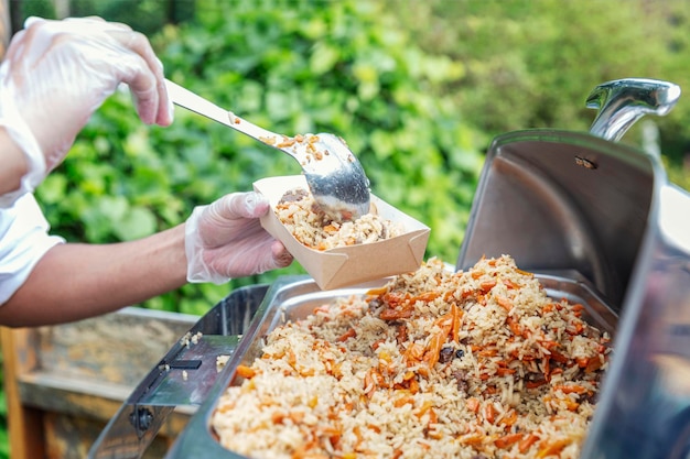 Het koken van voedsel in de natuur bij een picknick De handen van een man zetten rijst met vlees uit een voedselverwarmer in een kartonnen bord Closeup