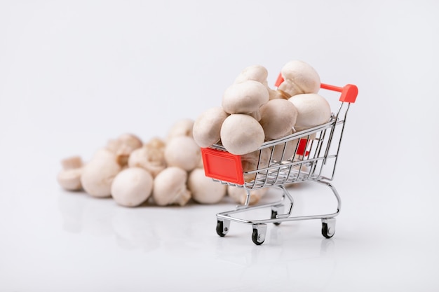 Het kopen van gezond voedselconcept. Winkelwagentje met champignons op grijze achtergrond.