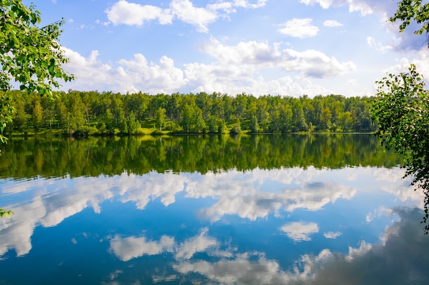 Het landschap van een pittoresk meer en de weerspiegeling van de bewolkte blauwe lucht en het bos.