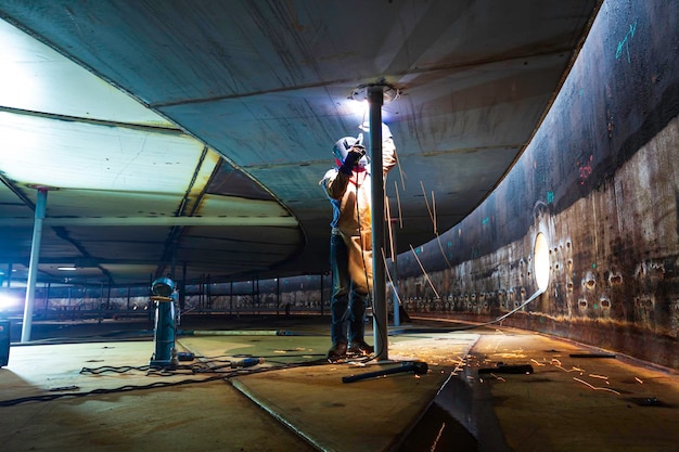 Het lassen van metaal van de mannelijke werknemer maakt deel uit van de constructie van de machineplaat, de tankbalk, flitsvonk in besloten ruimtes