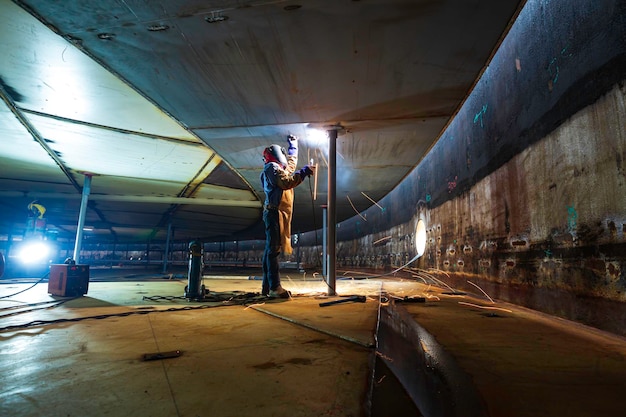 Het lassen van metaal van de mannelijke werknemer maakt deel uit van de constructie van de machineplaat, de tankbalk, flitsvonk in besloten ruimtes