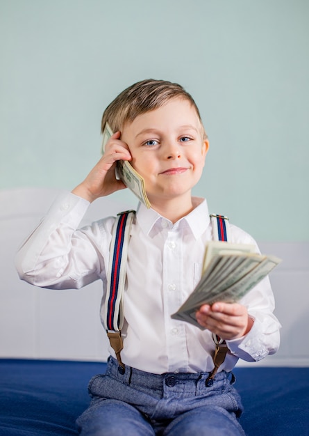 Het leuke babyjongen spelen met heel wat geld zoals het spreken op telefoon, Amerikaanse honderd dollars contant geld. Amerikaanse honderd dollar in contanten.