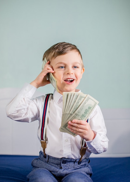 Het leuke babyjongen spelen met heel wat geld zoals het spreken op telefoon, Amerikaanse honderd dollars contant geld. Amerikaanse honderd dollar in contanten.